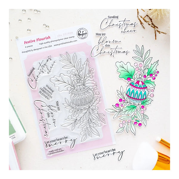 Festive Flourish clear stamp set by Pink Peony Studio, featuring Christmas-themed phrases and a holly ornament stamp, displayed on a white background with a pink ink pad and sample stamped designs.