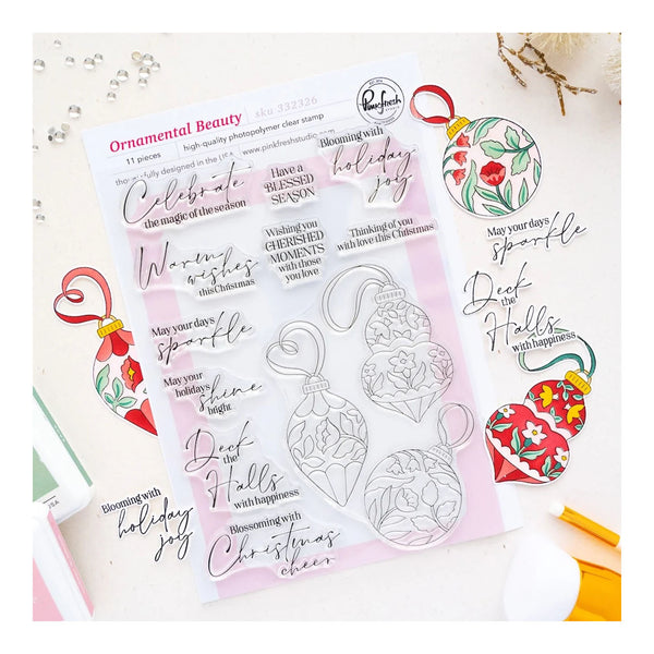 A sheet of clear photo stamping plates with holiday ornament and script stamp designs, displayed on a light surface with decorative Christmas ornaments and crafting tools around it. The sheet is branded 'Ornamental Beauty' and includes the 'Peaches' brand mark.