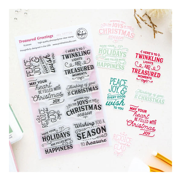 A sheet of clear stamp templates with holiday phrases, displayed on a white background alongside sample stamped impressions in pink, green, and red, with a pencil and decorative twine nearby.