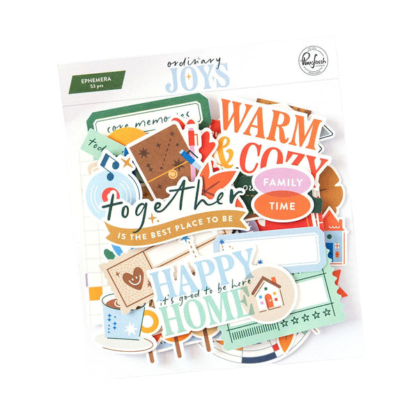 A sheet of assorted decorative stickers and small paper cutouts from Ordinary Joys, featuring warm autumn and cozy family-themed phrases like 'WARM & COZY', 'FAMILY TIME', and 'HAPPY HOME' in orange, teal, brown, cream, and blue tones.