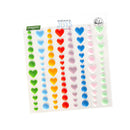 A sheet of colorful heart-shaped embellishments or stickers by Jojo's Ordinary Joys, featuring rows of 3D-effect hearts in various pastel and bright colors like green, blue, red, yellow, pink, and light green on a white backing card.