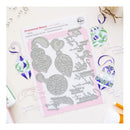 A flat-lay product photo of a metal die-cutting or stamping template sheet labeled 'Ornamental Beauty' with silver ornament-shaped dies on a pink backing card, surrounded by decorated oval and heart ornaments and craft papers on a light beige surface.
