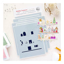 A flat-lay of crafting supplies on a white surface, featuring a stack of light blue stamping mats with dark navy house-shaped cutout templates, a printed card labeled Holiday Treasures, decorative dried flowers, and a small illustrated shelf sticker set.