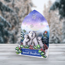 A Christmas-themed gift box or display stand featuring an illustrated winter scene with a polar bear family, snowflakes, mountains, and a robin, set on a light wood surface with a blurred snowy outdoor background.