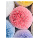 A close-up of fluffy yarn balls in soft pastel and bright colors, with a pink ball centered and other visible balls in white, yellow, blue, and lavender.