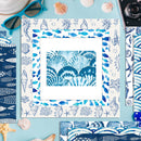 A square framed art print with a blue and white seashell and fish pattern border, featuring a central blue seashell illustration, styled on a light blue background with seashells, sunglasses, and a camera.