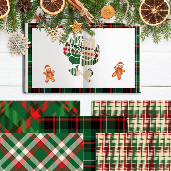 A flat-lay display of Christmas-themed paper products, featuring a 3D pop-up card with a green and red plaid border and gingerbread men, surrounded by flat sheets of matching plaid patterned paper. The scene is decorated with pine branches, dried orange slices, and wooden snowflakes on a white wood background.