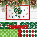 A Christmas-themed paper craft kit or scrapbook paper set displayed on a white wood background with holiday decorations. The main open booklet shows a green tree with a Santa Claus figure inside, surrounded by red and green festive patterns.