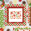 A flat-lay display of various Christmas-themed patterned papers and cardstock sheets arranged on a light wood background, featuring festive designs like gingham, holiday motifs, and gingerbread illustrations.