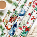 Six rolls of Christmas-themed wrapping paper are arranged diagonally on a white surface, decorated with festive watercolor illustrations including pine trees, holly, ornaments, stars, and deer. A cup of coffee and a knitted sweater are styled as props in the corners.