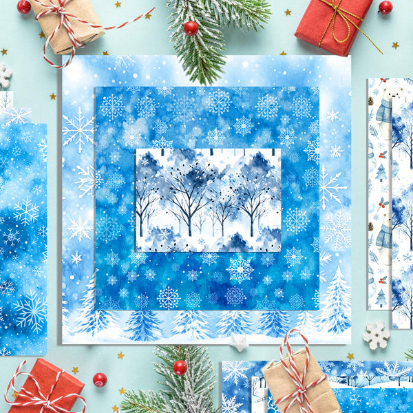 A flat-lay display of blue winter-themed scrapbooking papers with snowflakes, trees, and snowy pine trees, styled with Christmas gifts, evergreen branches, and red berries on a light blue background.