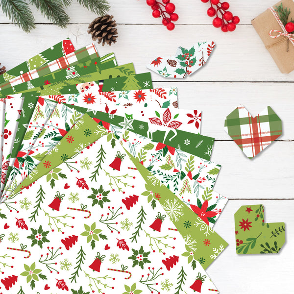 A styled flat-lay of multiple sheets of Christmas-themed patterned paper on a white wood background, surrounded by holiday props like pine branches, a pinecone, red berries, and a small kraft gift box.