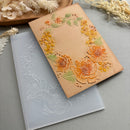 A floral embossed kraft paper card or envelope placed on top of a translucent silicone mold, styled with dried flowers on a gray surface.