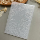 A translucent silicone mold with embossed floral and bird designs, displayed on a neutral gray surface with dried floral props.