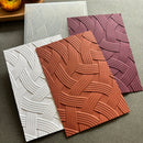Three textured rectangular tiles with an embossed basketweave pattern in white, terracotta orange, and dusty purple, arranged on a gray surface.