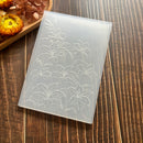 A translucent silicone mold with embossed lily of the valley floral patterns, displayed on a dark wood background with dried flowers in the corner.
