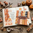 Scrapbooking paper sheets with autumn-themed designs on a wooden surface with decorative items.