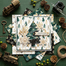 A layered Christmas greeting card with gold snowflakes, green pine trees, and a 'Wishing You A CELESTIAL CHRISTMAS' banner, styled in a flat lay on a dark green wooden background with vintage toy trains, pinecones, a key, beads, and a small camera.