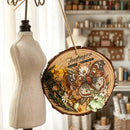 A round wooden slice wall hanging with a butterfly and floral design, suspended by a twine string in a softly styled craft or sewing room. A fabric dress form stands beside it.