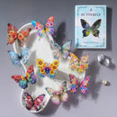 A flat-lay of the 'Butterfly' card game, showing the light blue card box with a butterfly illustration, a white shoe-shaped tray holding several colorful butterfly cards, and decorative crystals on a gray background.
