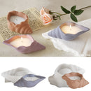 Three clam-shell-shaped candle holders in peach, lavender, and gray-blue are shown lit on a styled tabletop with a flower and paper, plus a smaller inset showing additional color options on a white background.