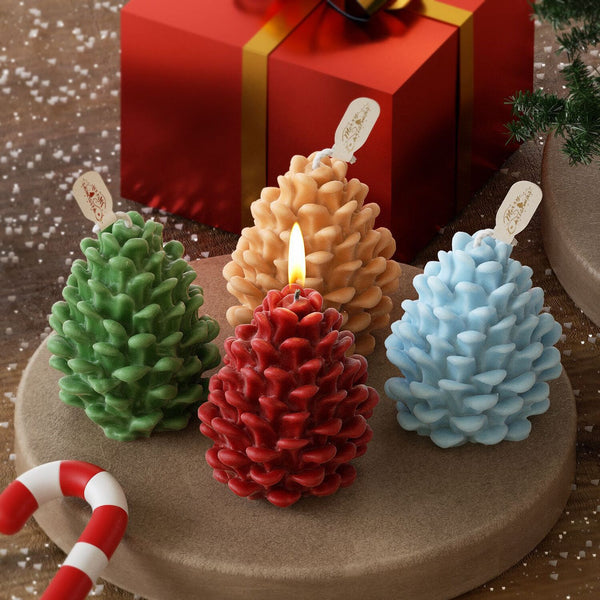 Four pine cone-shaped candles in green, beige, red, and blue on a decorative stand with a red box and candy cane in the background.