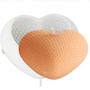A heart-shaped novelty candle in front of a white heart-shaped mold or tray. The candle has a textured honeycomb pattern and is a warm peachy-orange color, with a small white label on top.
