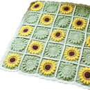 A handmade crocheted square blanket featuring a grid of sunflower motifs in yellow, brown, and green, finished with a white scalloped edge.