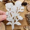 Metal floral cutting die held by a hand on a wooden surface with natural elements.
