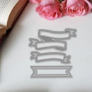 Metal die cutters shaped like banners on a white surface with pink roses and an open book.
