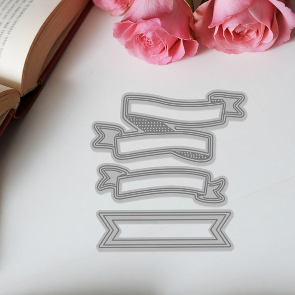Metal die cutters shaped like banners on a white surface with pink roses and an open book.