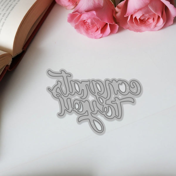 Decorative metal word die on a white surface with pink roses and an open book in the background.