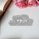 Decorative word die cut on paper with pink roses and an open book in the background