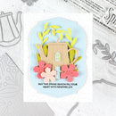 A handmade spring-themed greeting card featuring a beige teapot with a window, yellow-green leaves, pink and peach flowers, and the text 'MAY THIS SPRING SEASON FILL YOUR HEART WITH RENEWED JOY.' The card is displayed on a white background with crafting dies and metal templates around it.