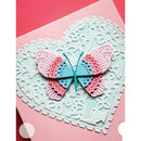 A handmade layered paper butterfly embellishment in pink and light blue, layered over a large white embossed heart-shaped lace pattern on a pink cardstock background.
