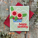 A handmade birthday card featuring a blue patterned teacup filled with pink and red flowers and green leaves, placed on top of a red envelope over a rustic wood surface with decorative greenery.