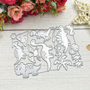 A set of dinosaur-themed metal cutting dies arranged on a white wooden surface, surrounded by decorative pink flowers and a woven star ornament.