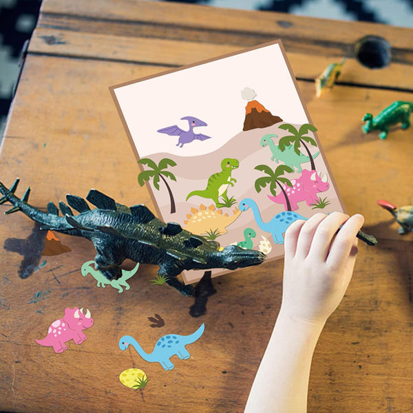 A child's hand is holding a dinosaur toy next to a colorful dinosaur activity card on a wooden table, with other loose dinosaur cutouts and a toy around.