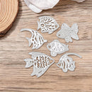 Six white laser-cut metal fish dies with detailed tropical fish patterns, arranged on a light brown wooden surface.