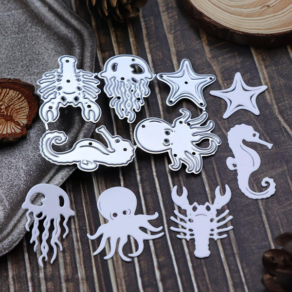 A set of white metal cutout templates featuring various sea life designs including an octopus, seahorse, starfish, jellyfish, and crab, arranged on a dark wood background with decorative props.