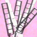 Four black metal film strip frames with perforations, arranged diagonally over white paper strips on a pink background with subtle gold glitter.