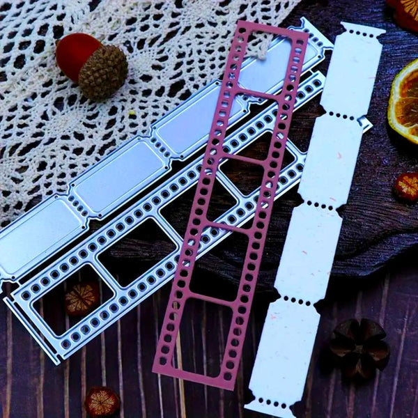 A metal die-cut craft cutting template set displayed on a dark wooden surface with decorative props including a lace doily, acorns, and dried orange slices. The set includes a silver-colored frame template, a dusty rose/pink frame template, and several white paper transfer sheets.