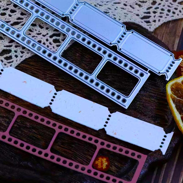 Two metal die-cut stamping templates, one silver and one rose gold, displayed on a dark wooden background with a white lace doily and dried orange slices.