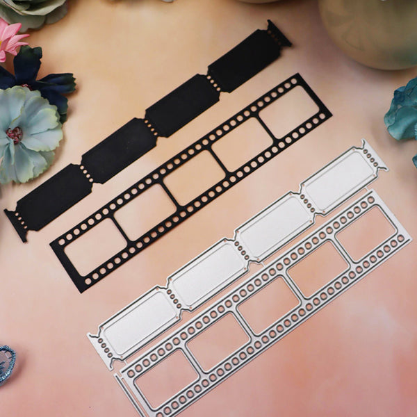 Three metal die-cut craft templates shaped like vintage film reels are arranged on a soft peach background with decorative flowers in the corners. One template is black, and two are silver-colored metal.