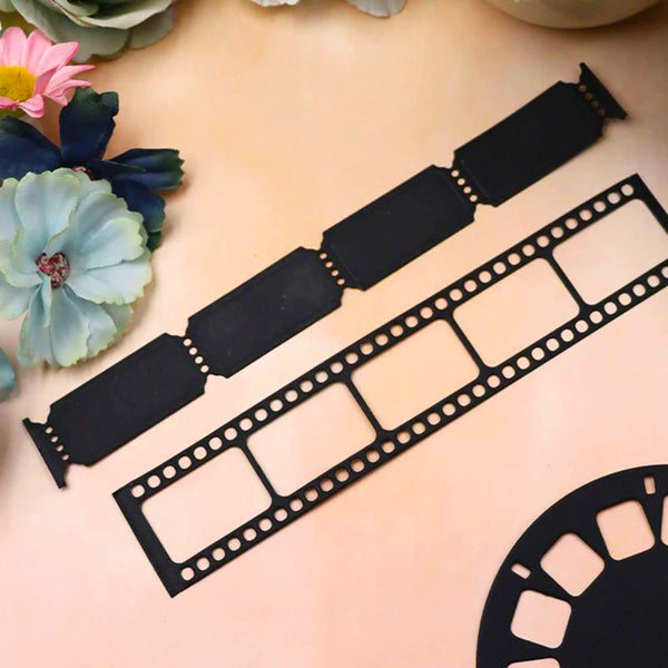 Black metal film strip cutouts, including a full-length strip and a partial reel section, arranged on a peach-colored surface with decorative flowers in the corner.
