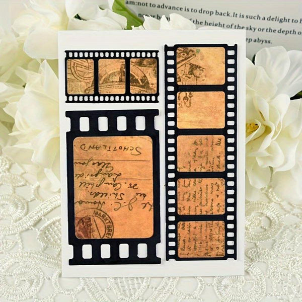 A square white card featuring a vintage film strip design with antique-style tan paper inserts, handwritten script, and postage stamp motifs, displayed on a white lace surface with white flowers in the background.
