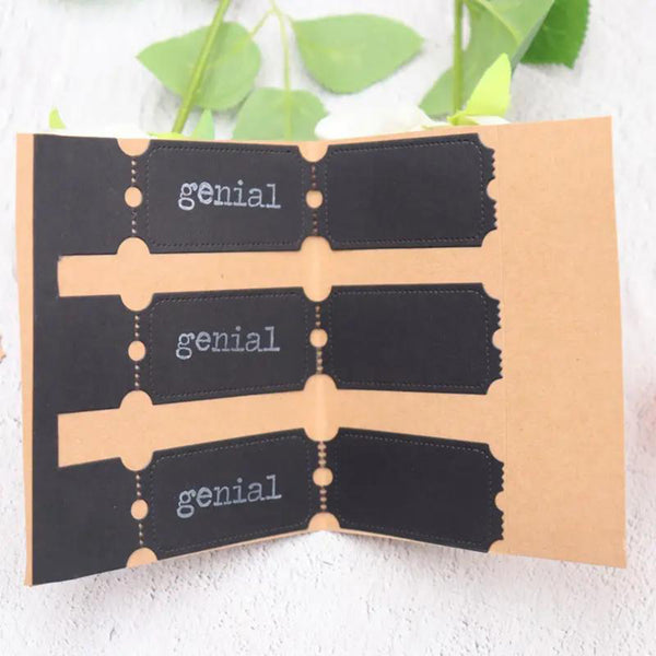 A handmade paper book or journal shown open, featuring three black tabs printed with the word 'genial' in white typewriter font, set against a light textured background with green leaves at the top.