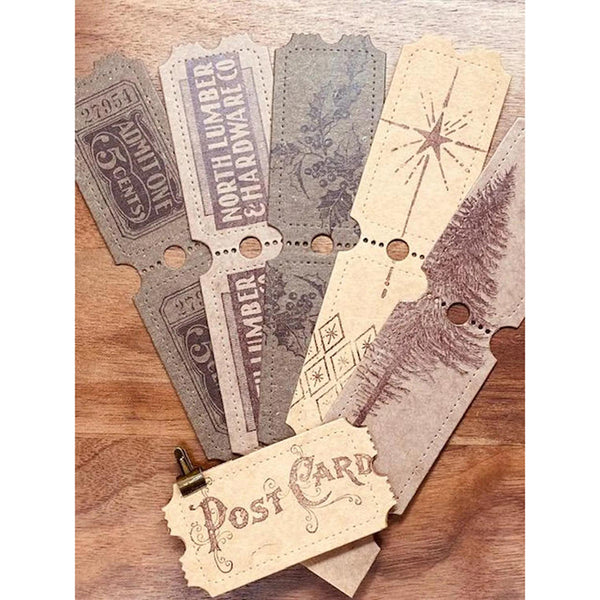 A set of vintage-style paper postcard designs fanned out on a wooden surface, featuring distressed text, starburst motifs, and tree illustrations in muted beige, gray, and brown tones.