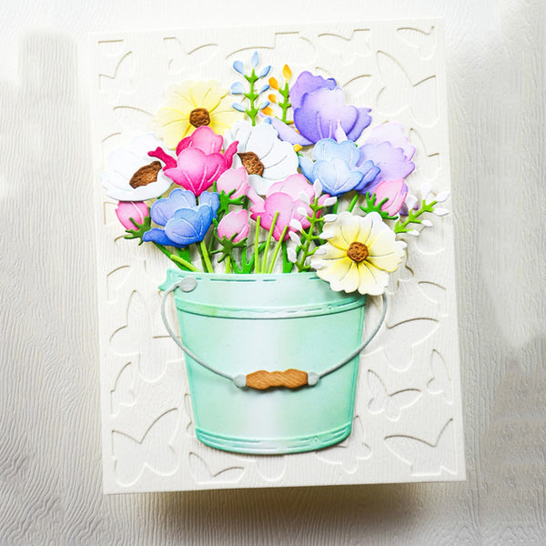 A square handmade card featuring a mint green bucket filled with colorful artificial flowers, set against a white embossed floral background.