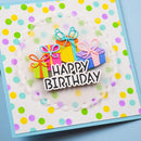 A square handmade-style birthday card with a white base decorated with multicolored polka dots, featuring three colorful gift boxes with bows and the words 'HAPPY BIRTHDAY' in white letters with black outlines. The card is photographed at an angle on a light blue background.